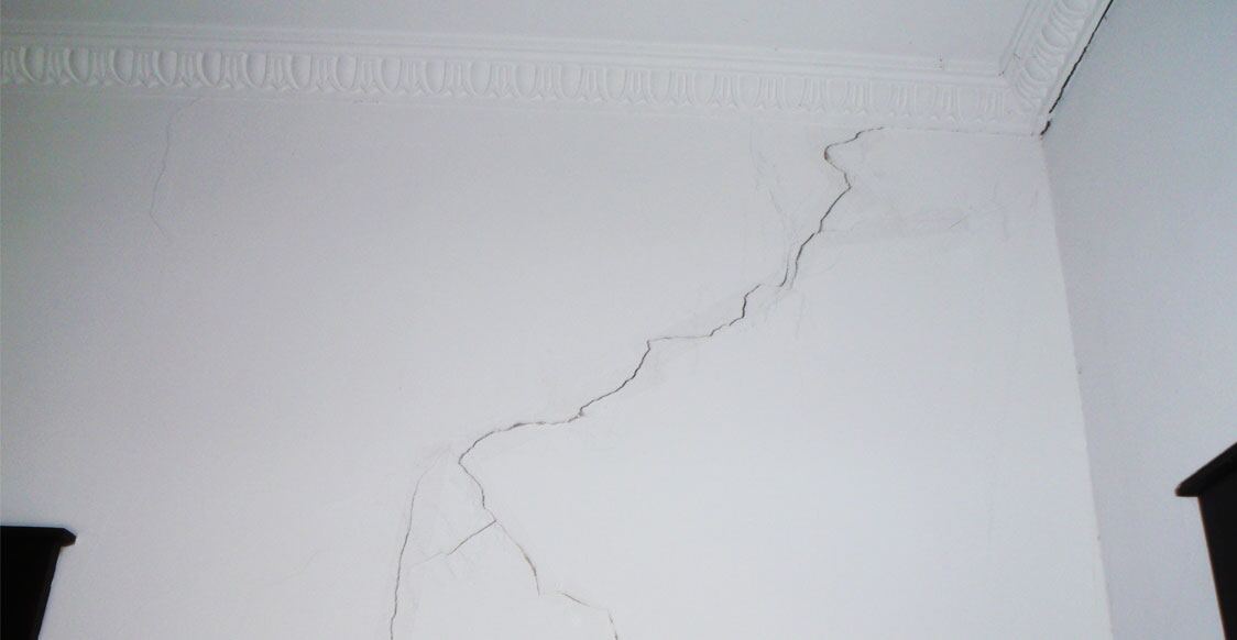 A crack running across a white plaster wall, photographed before repair and repainting