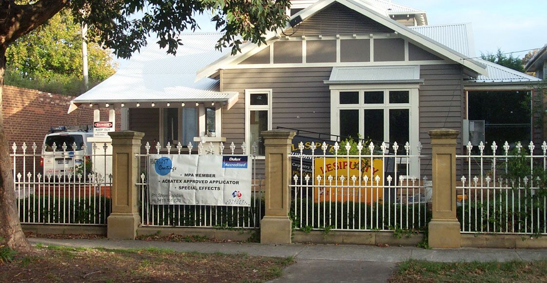 A weatherboard bungalow behind a white picket fence during an exterior repaint