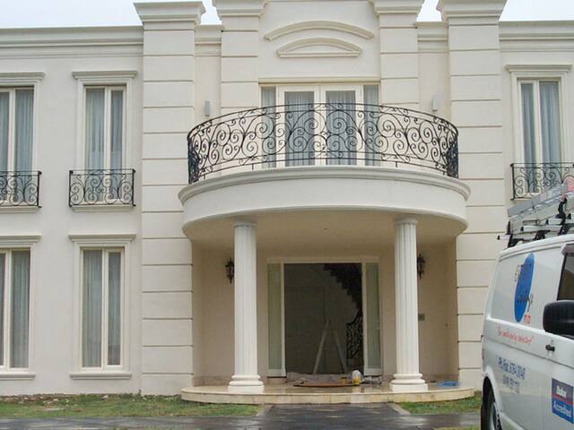 A grand two-storey rendered home with a curved balcony, freshly painted in cream