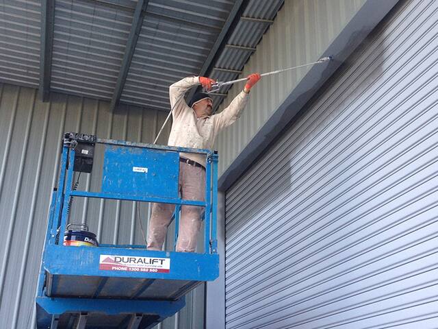 A painter on an elevated work platform repainting the metal cladding of a warehouse