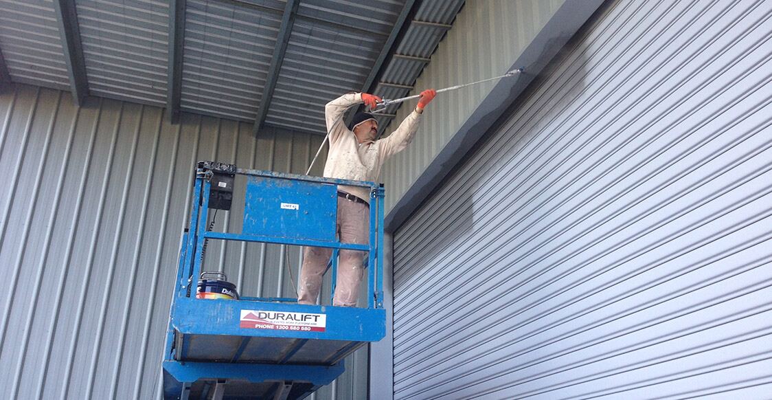 A painter on an elevated work platform repainting the metal cladding of a warehouse